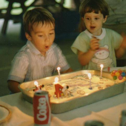Scott blowing out candles on a birthday cake with a friend.